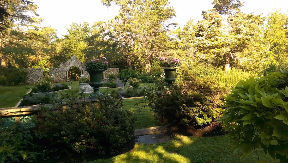 Well-kept garden with a stone arch, urn planters, and lush trees.