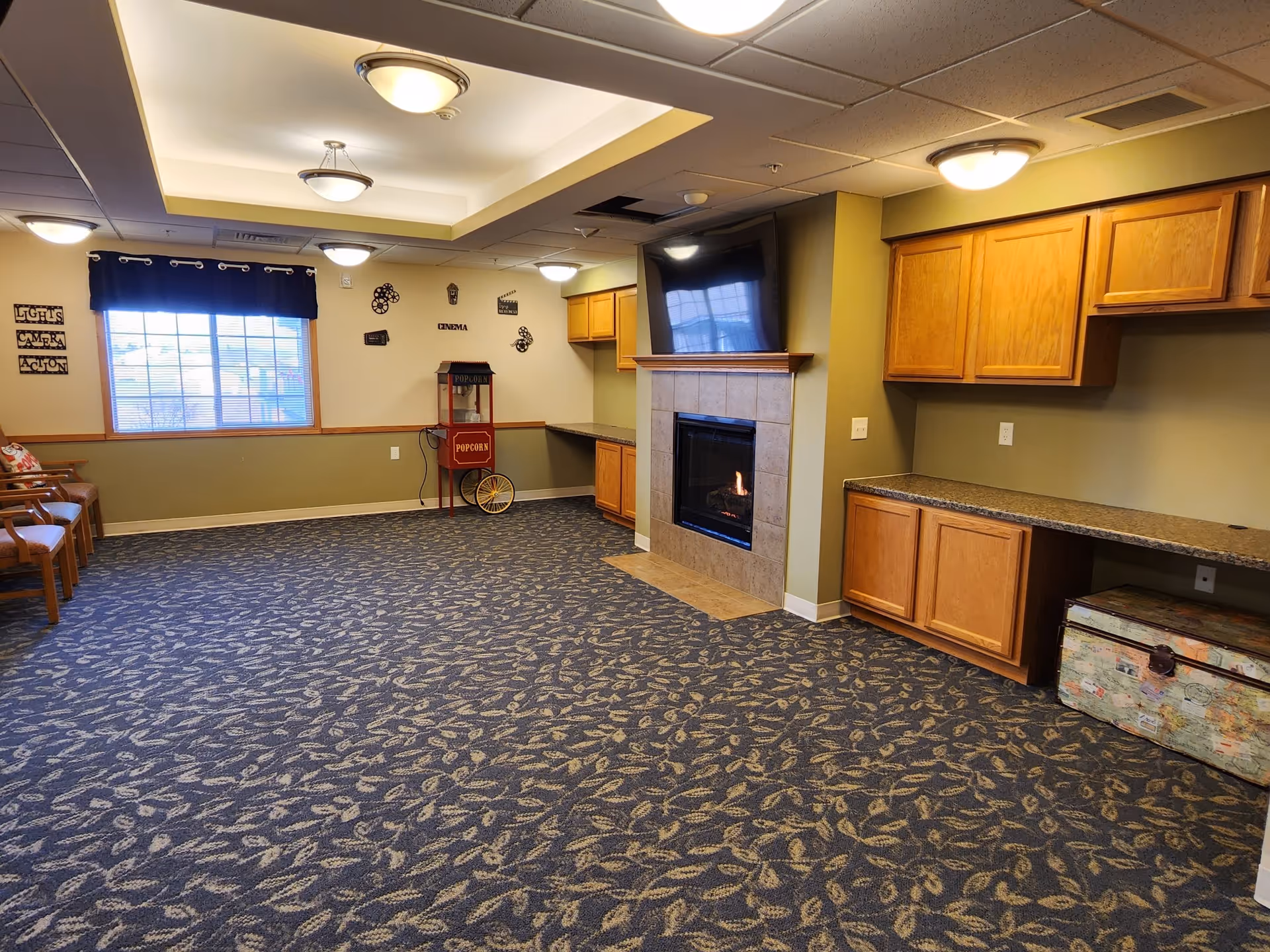 Spacious senior living lounge with a fireplace, wooden cabinets, countertops, and decorative wall accents.