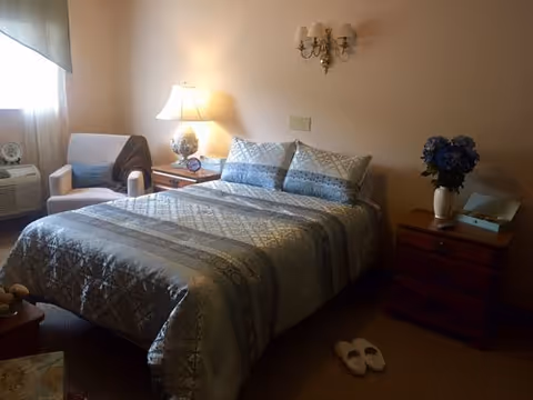 A cozy bedroom in a senior living facility with a bed, lamps, and nightstands.