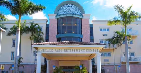 Front view of Emerald Park Retirement Center entrance with palm trees and blue sky.