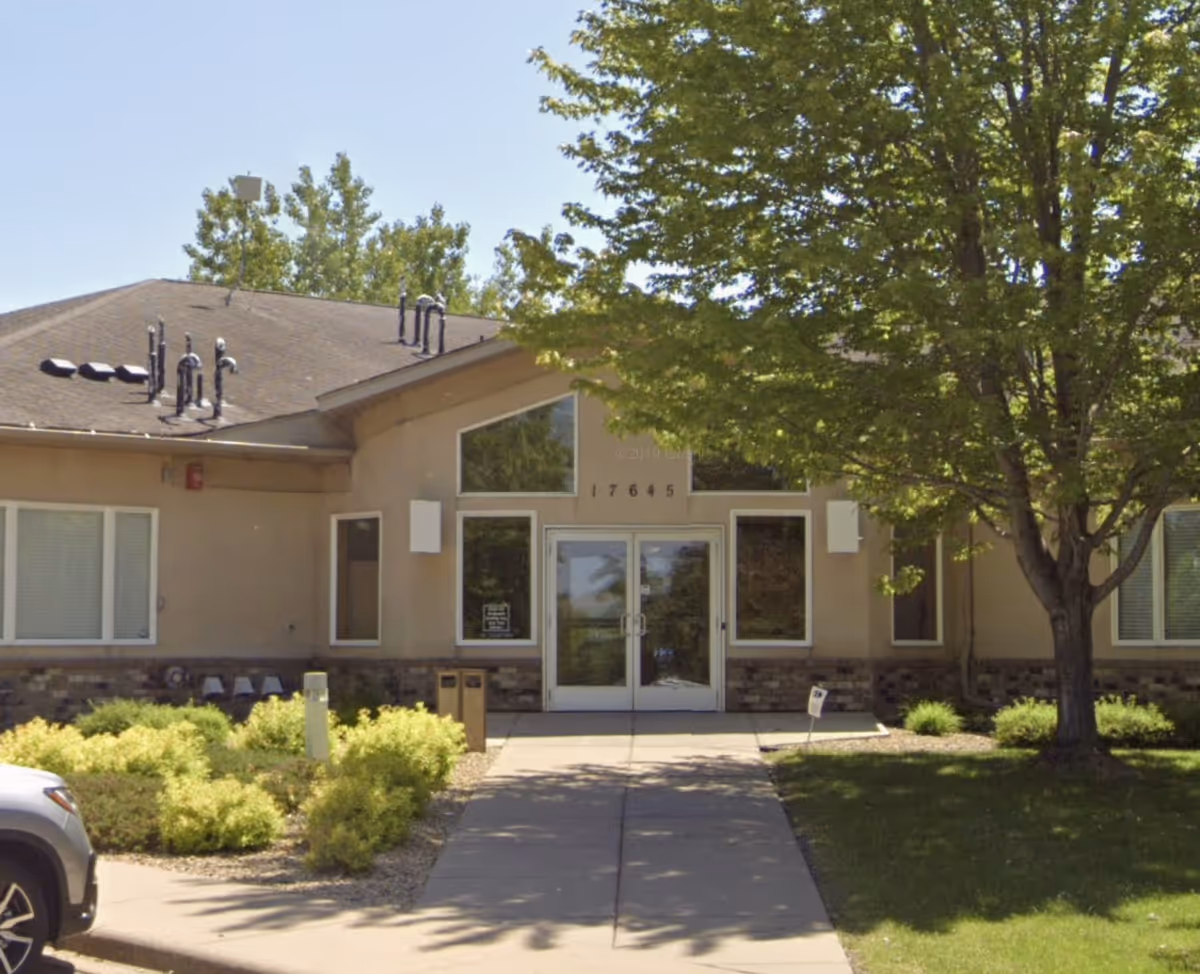Front exterior of Minnesota Hospice with glass doors, walkway, and trees.