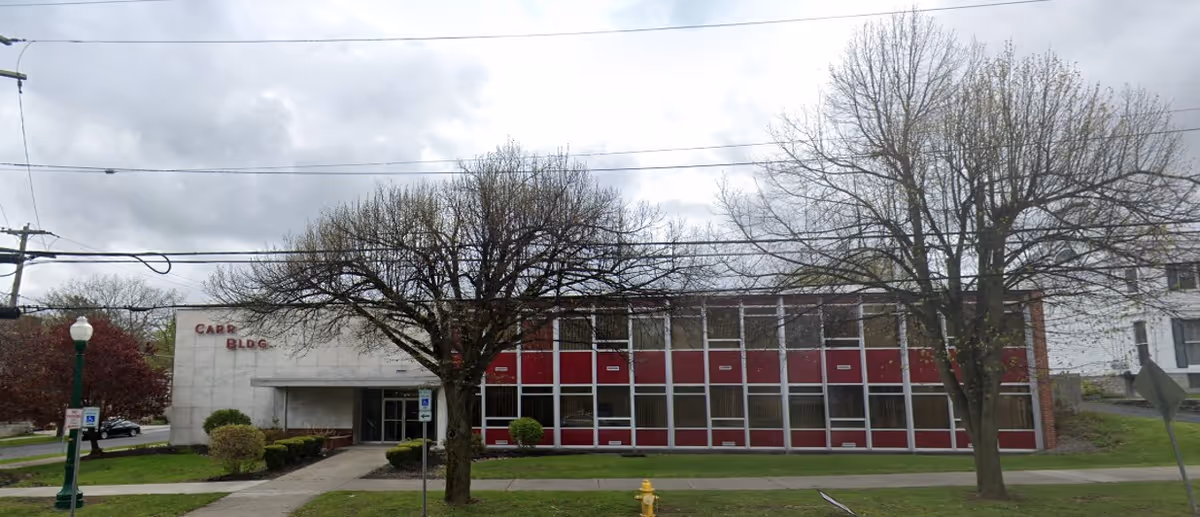 Exterior front view of a low-rise building with large windows and leafless trees.