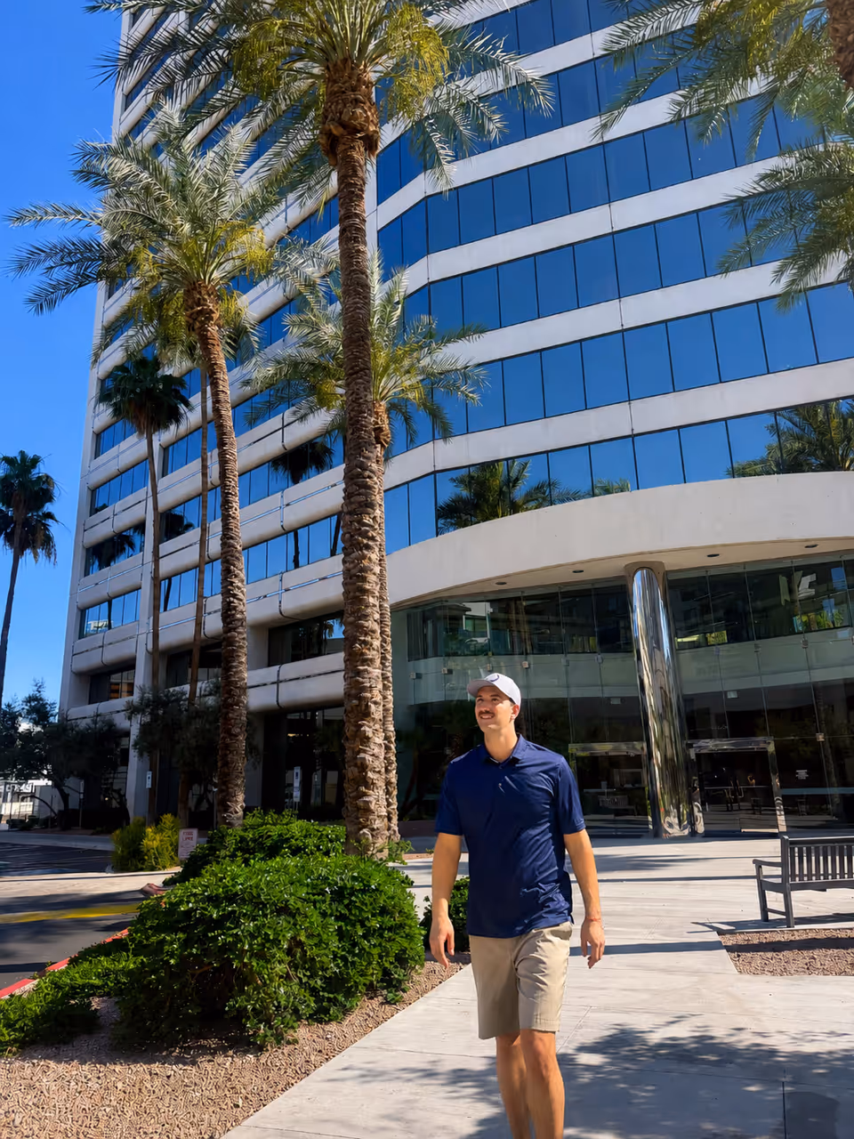 Tall glass-front building with palm trees and a man walking outside near the entrance.