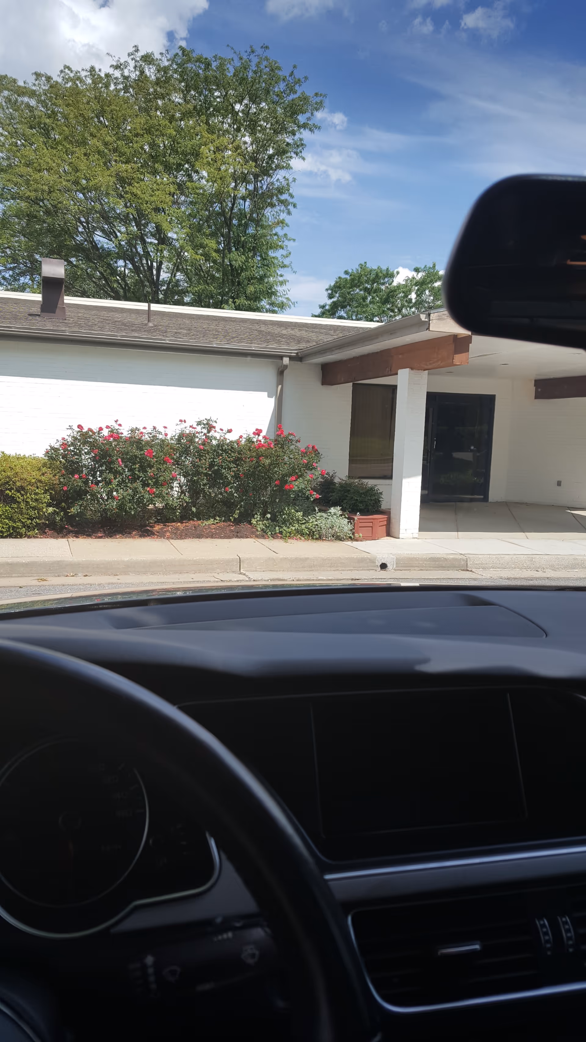 Car dashboard foreground; exterior view of a senior living facility entrance.