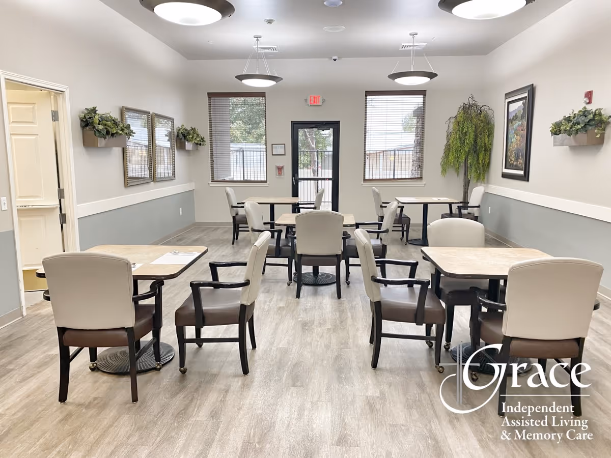 Bright dining room with several tables and cushioned chairs in a Grace Assisted Living facility.