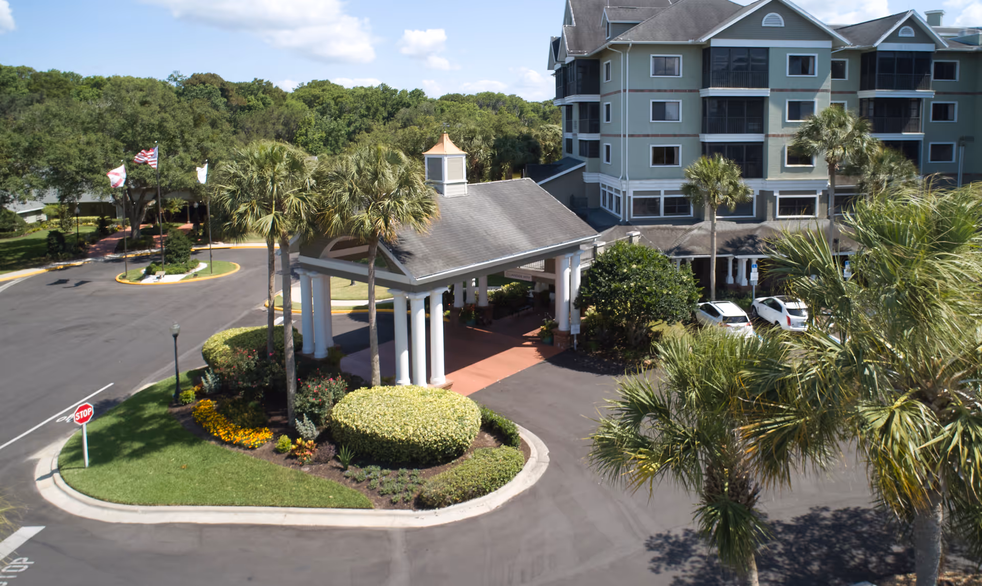 Front entrance of Lake Port Square with a porte-cochere, landscaped roundabout, palm trees, and a multi-story building.