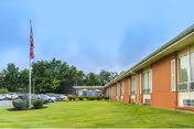 Exterior view of The Waters Of Springfield, a brick senior living facility with flagpole and parking.