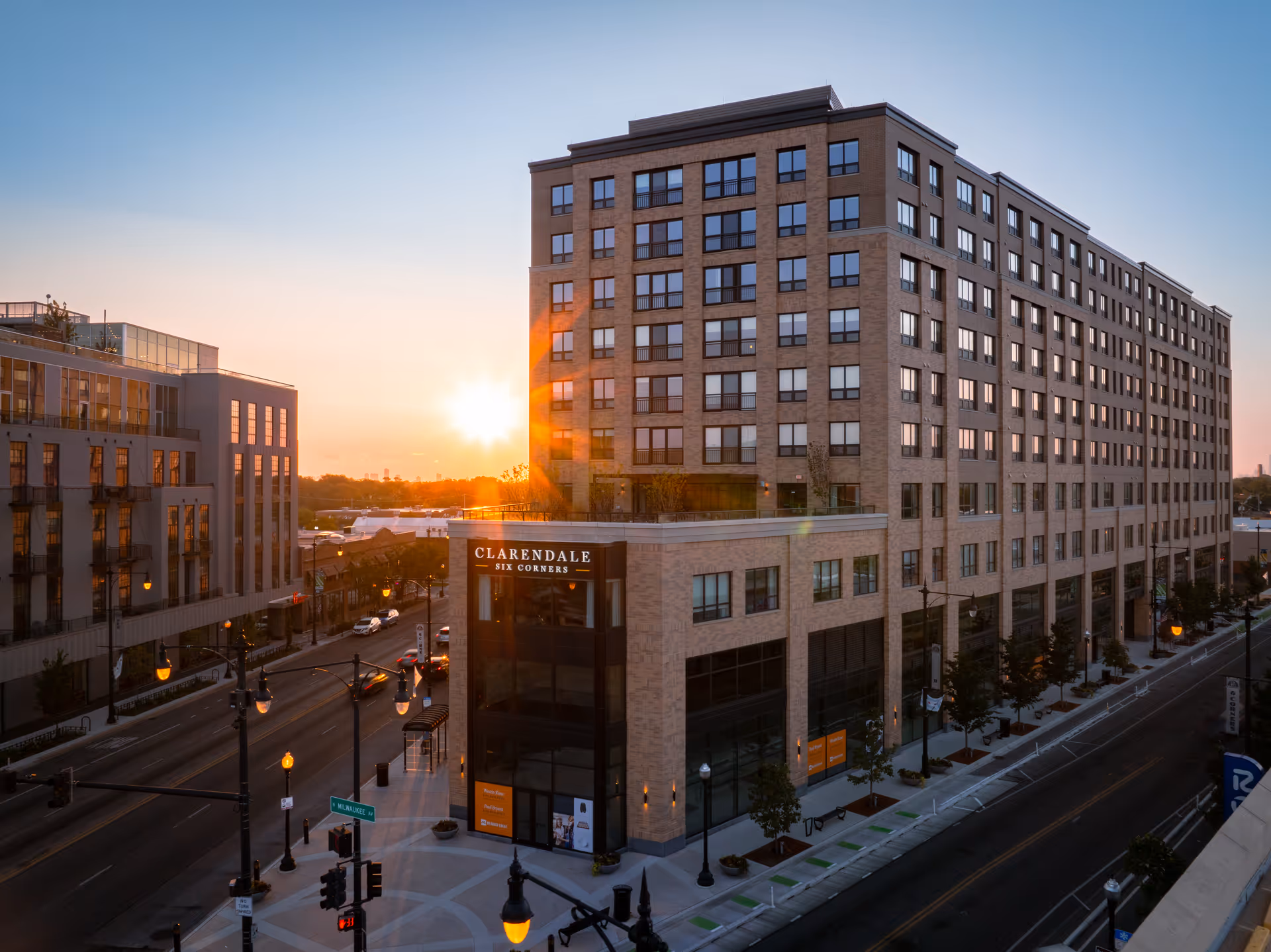 A multi-story Clarendale Six Corners senior living building at sunset along a busy city street.