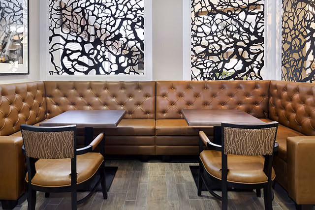 L-shaped brown leather tufted seating surrounds two tables in a modern lounge.