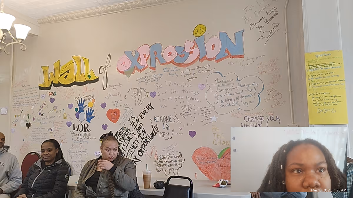 Indoor room with a large colorful mural reading Wall of Expression and seated residents.