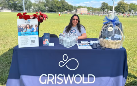 Staff sits at a Griswold booth at an outdoor park with promotional materials.