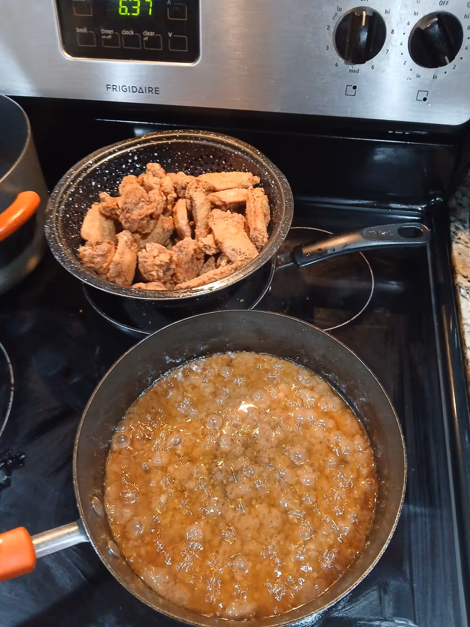 Stovetop kitchen scene with a frying pan of fried chicken and a bubbling sauce.