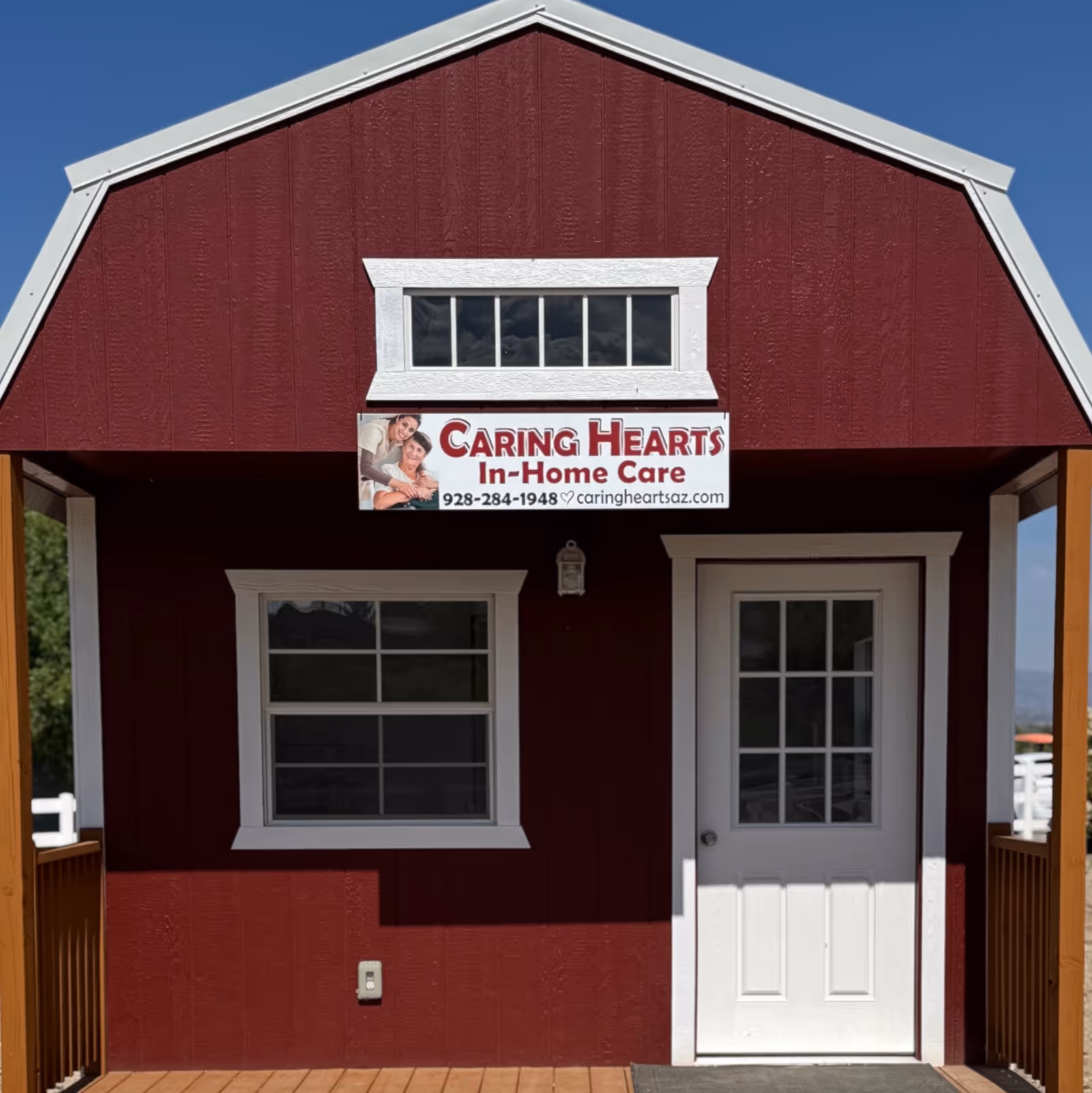 Red building front with Caring Hearts In Home Care sign, white framed window, and door.