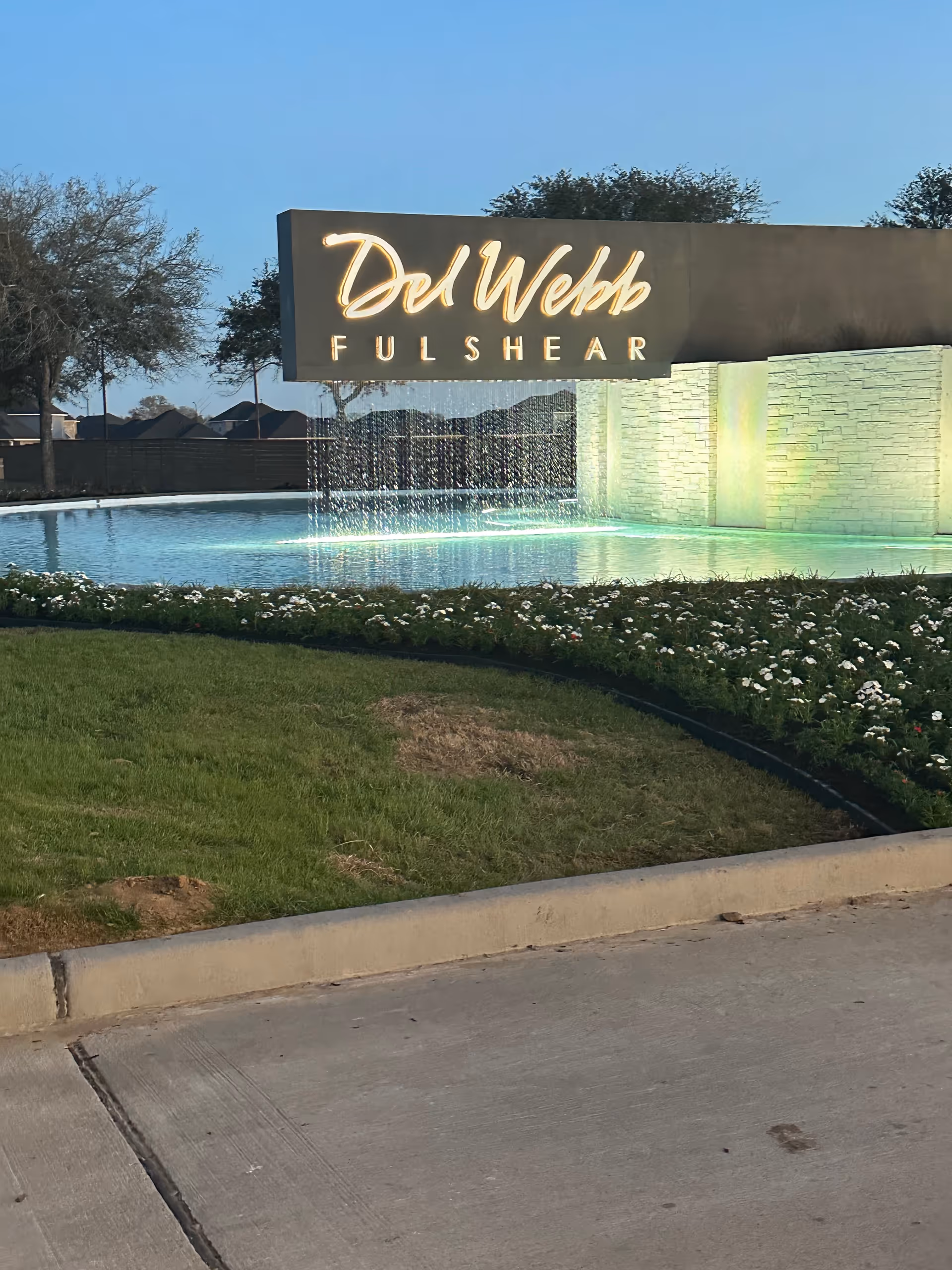 Del Webb front sign with illuminated logo and water feature at entrance.