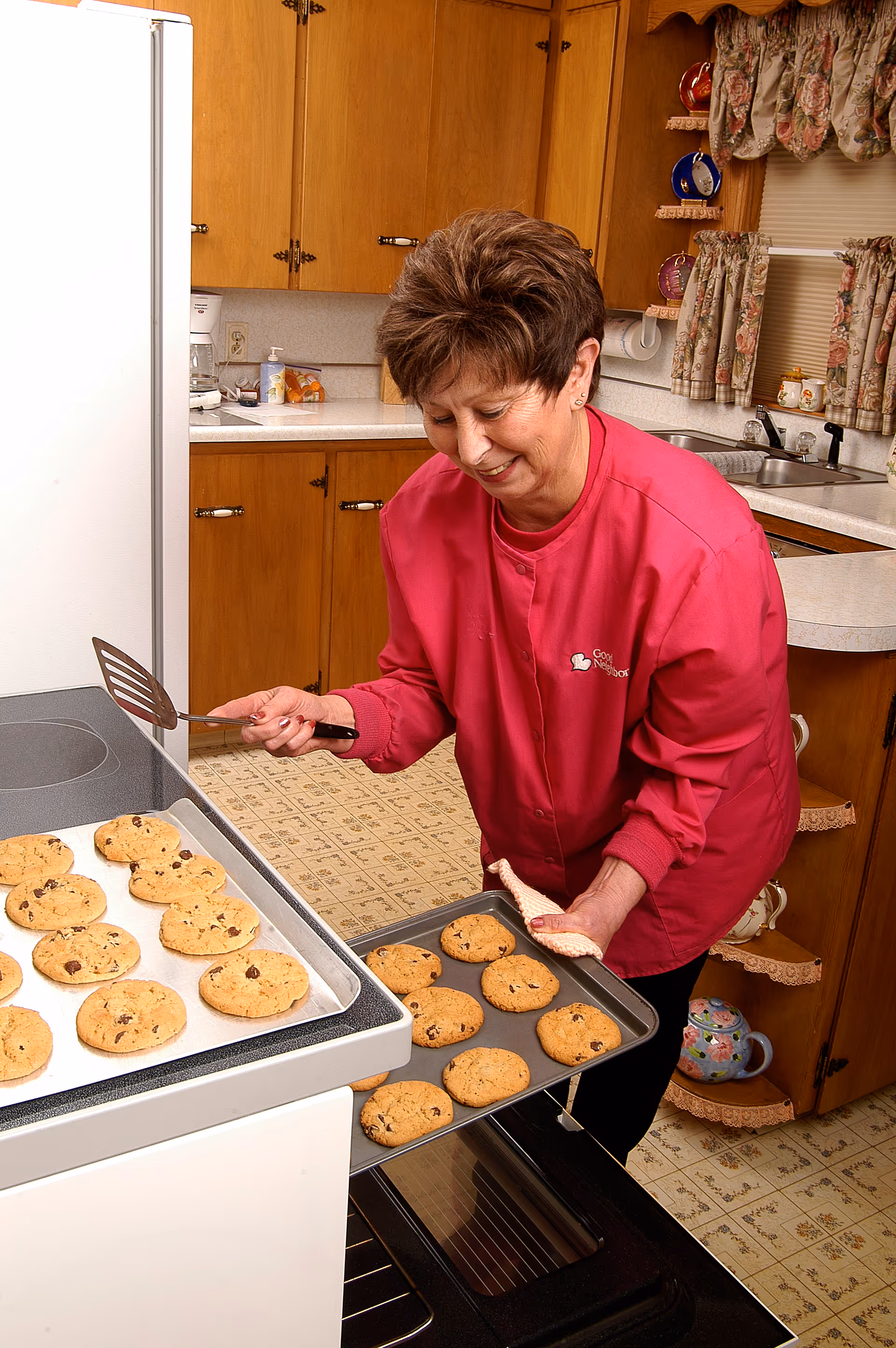 Caregiver in pink uniform bakes cookies in a kitchen, removing a tray from the oven.