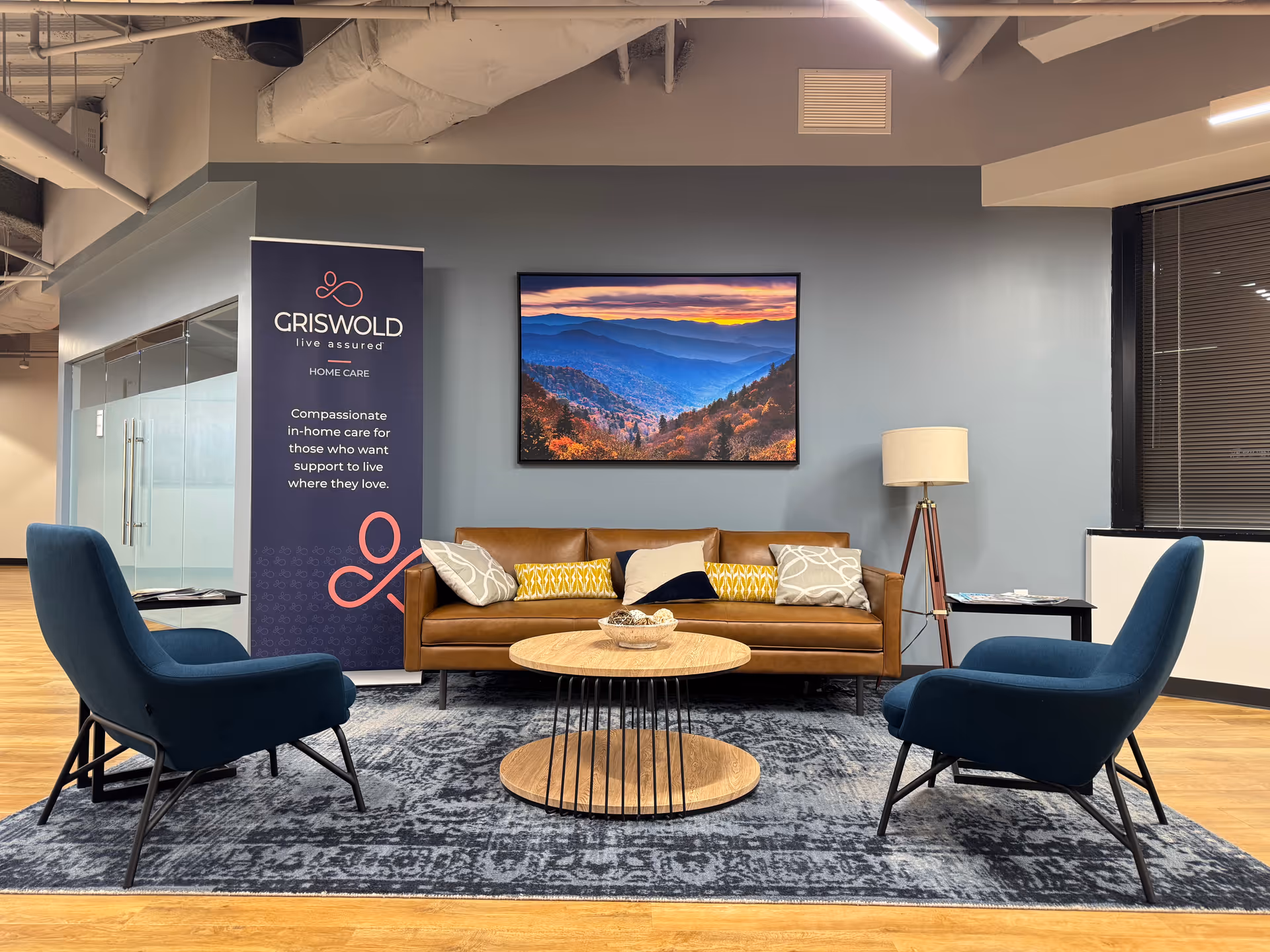 Modern lounge area with blue chairs, brown sofa, coffee tables, and a Griswold banner.