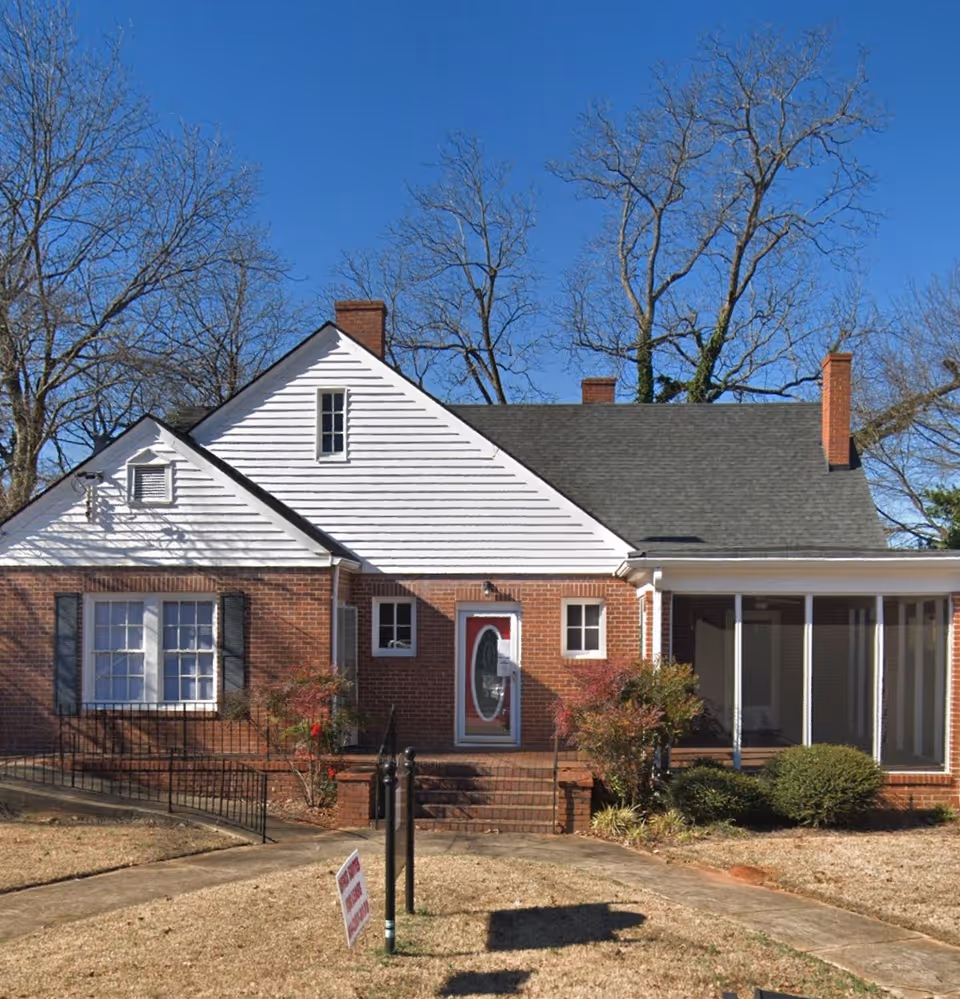 Brick and white house style senior living building with a red front door and steps.