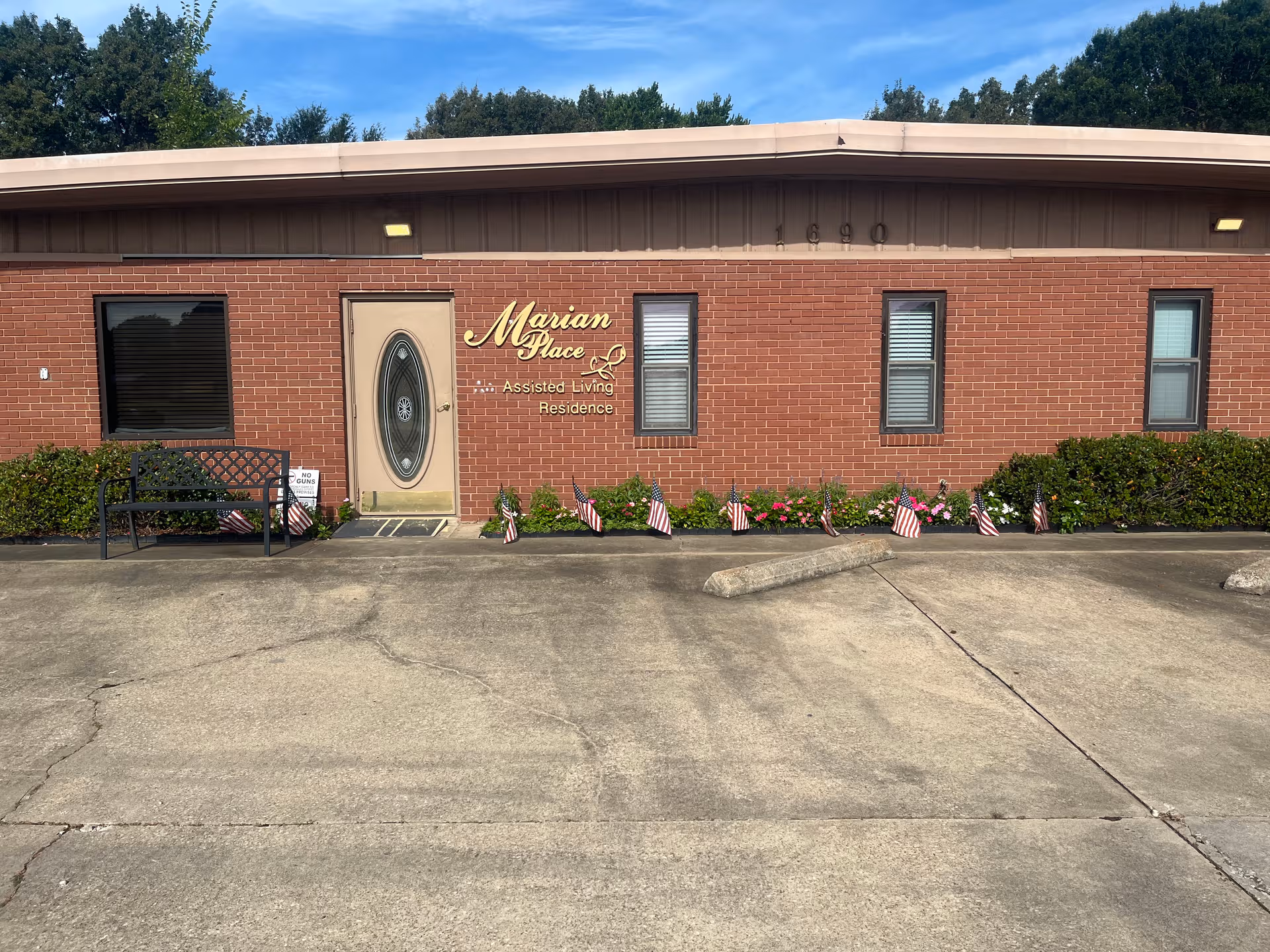 Front view of Marian Place Assisted Living building with sign, windows, bench, and American flags.