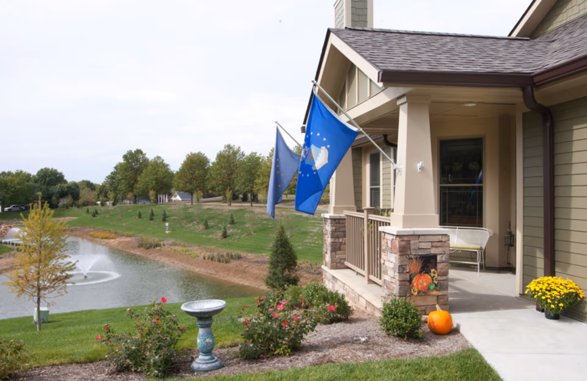 Front porch of Friendship Village Sunset Hills with flags, pumpkins, and a pond