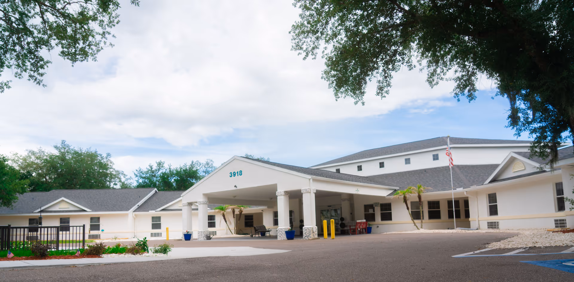 White senior living facility with a covered entrance, columns, and a flagpole outdoors.