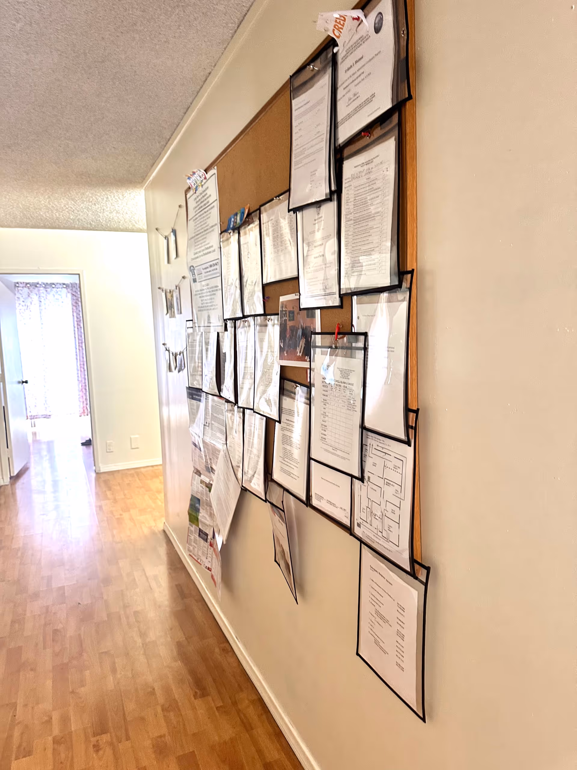 Narrow hallway with a corkboard filled with documents and notices on the wall.