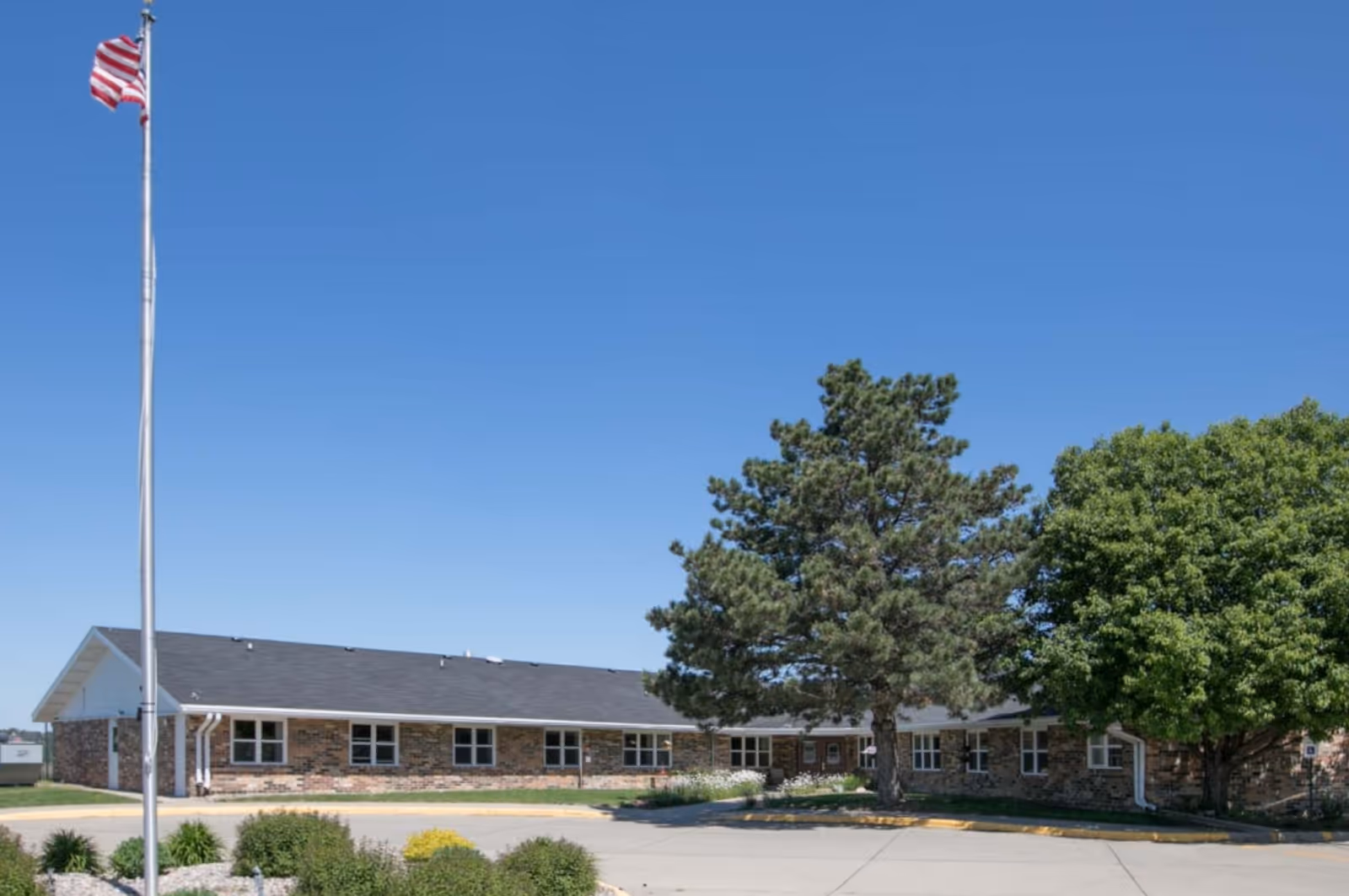 Front view of Mica Hill Estates, a single-story brick senior living building with flagpole