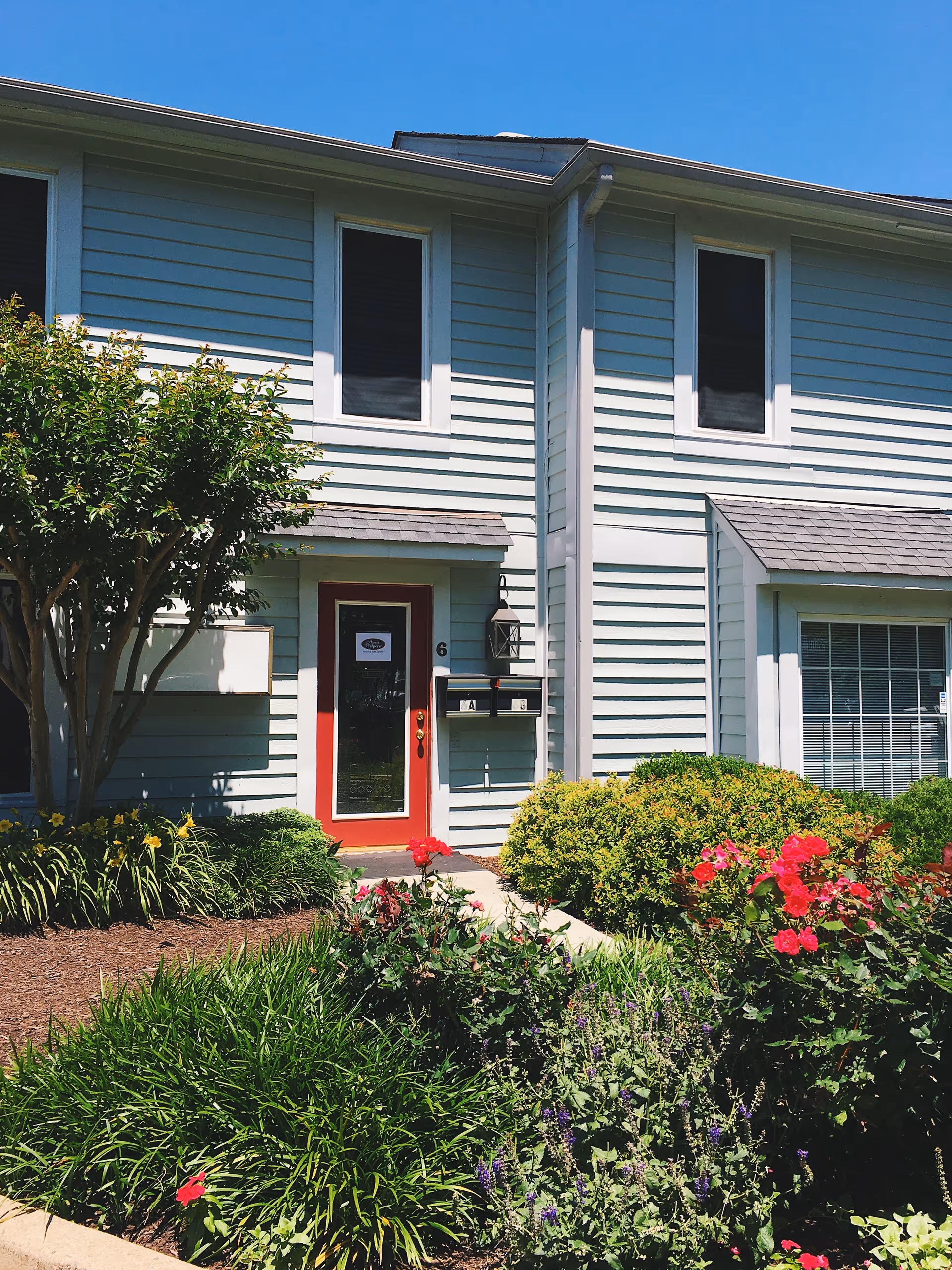 Blue two-story building with white trim, red front door, and lush landscaping.
