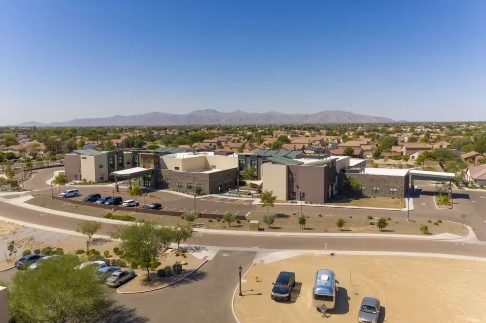 Aerial view of Surprise Health & Rehabilitation Center, a low-rise modern building with a parking lot, surrounding homes, and distant mountains.