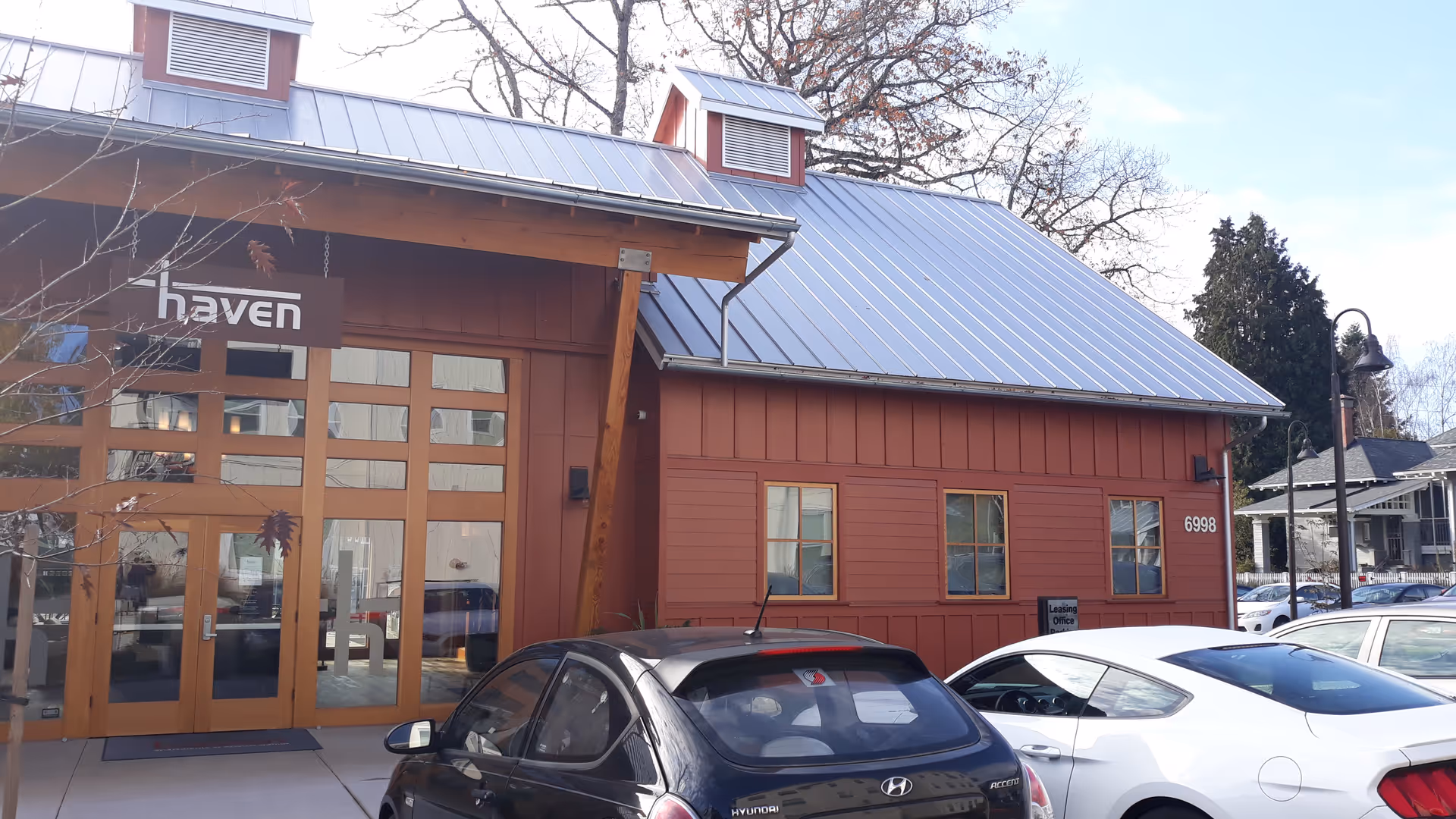 Red wooden building with metal roof, glass doors, and parked cars in front.