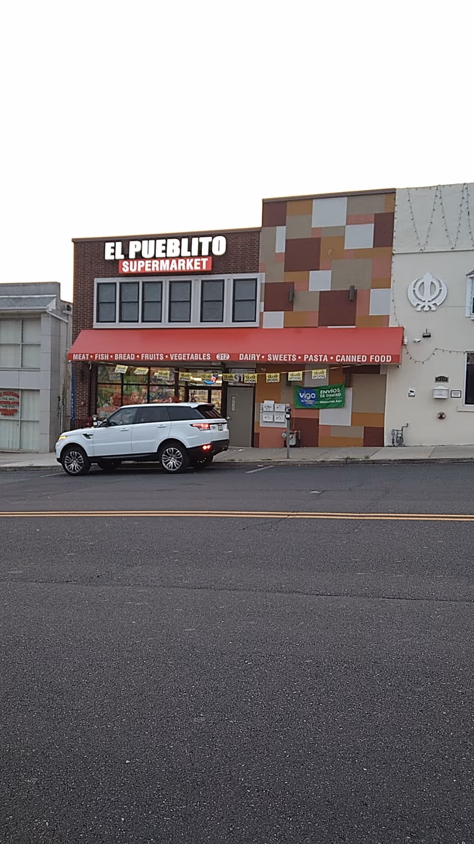 Exterior view of El Pueblo Supermarket storefront with a white SUV parked in front