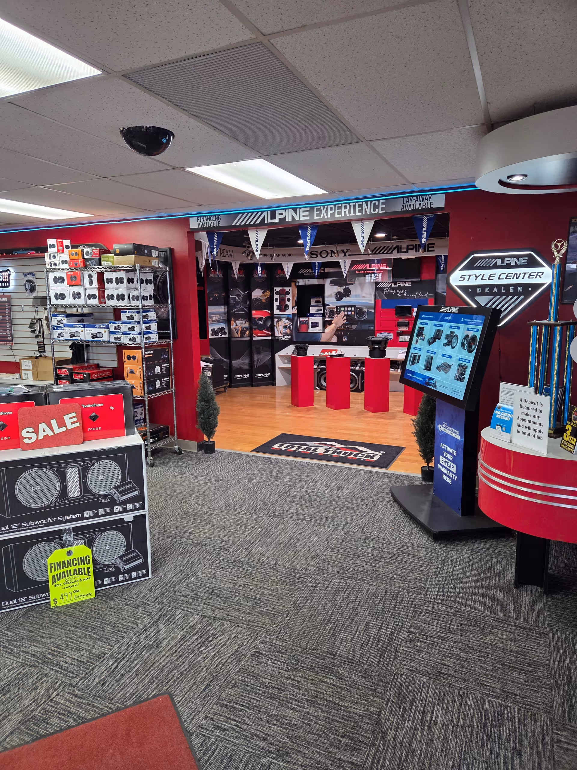 Interior of a retail electronics store with shelves, sale signs, and display screens.