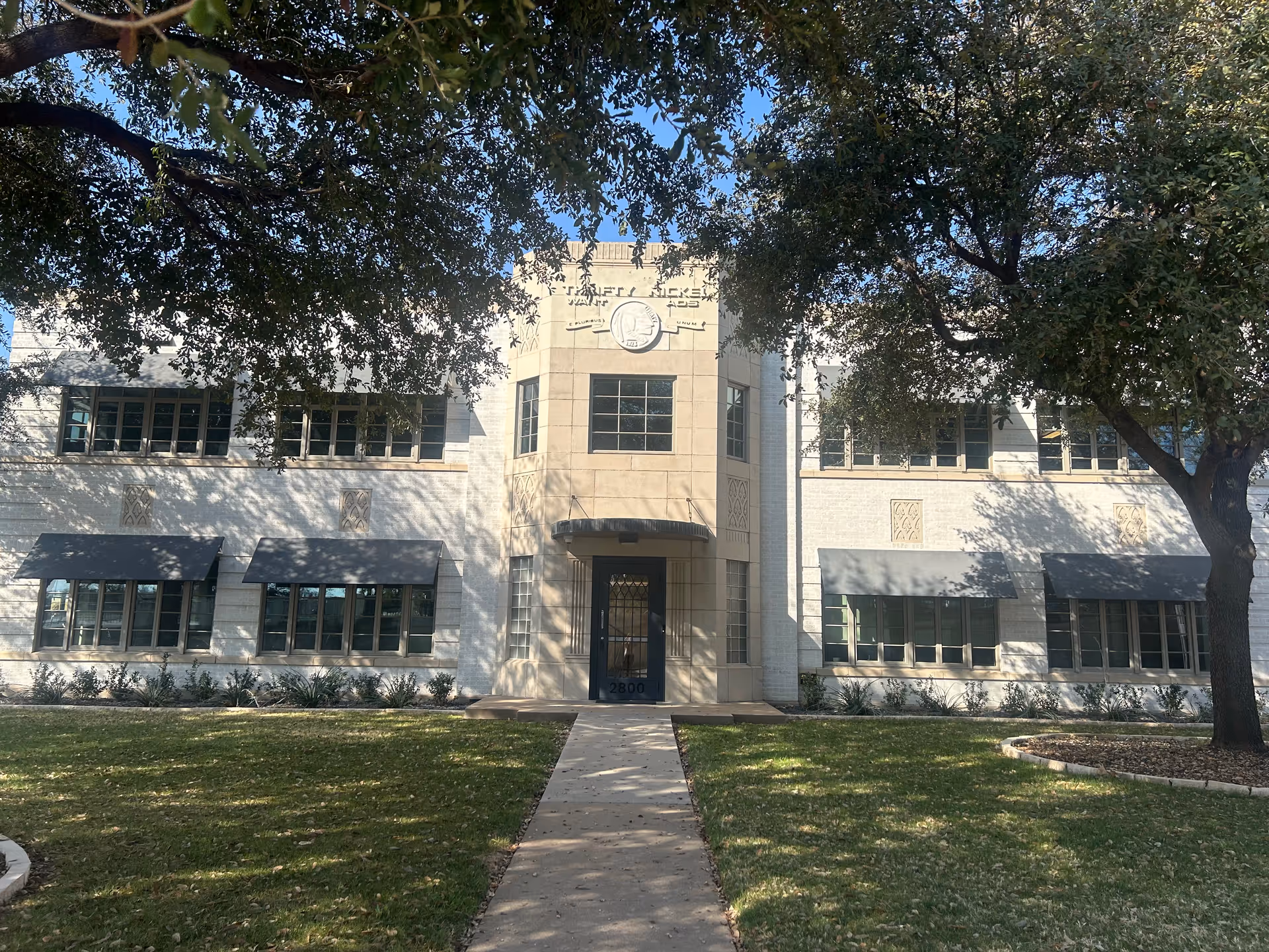 Two-story white brick senior living facility with central entrance and surrounding lawn.