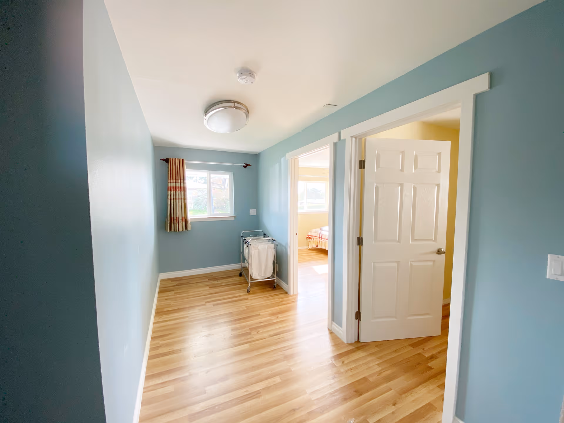 Blue-walled hallway with doorway to a bedroom and a rolling cart.