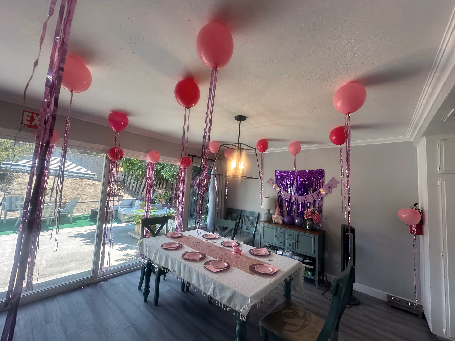 Decorated dining room with pink balloons, banner, and a table set for celebration.