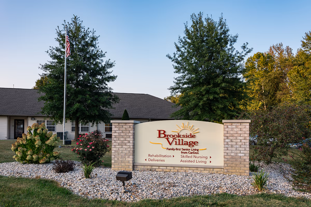 Brookside Village senior living exterior with sign, flagpole, and landscaped entrance.