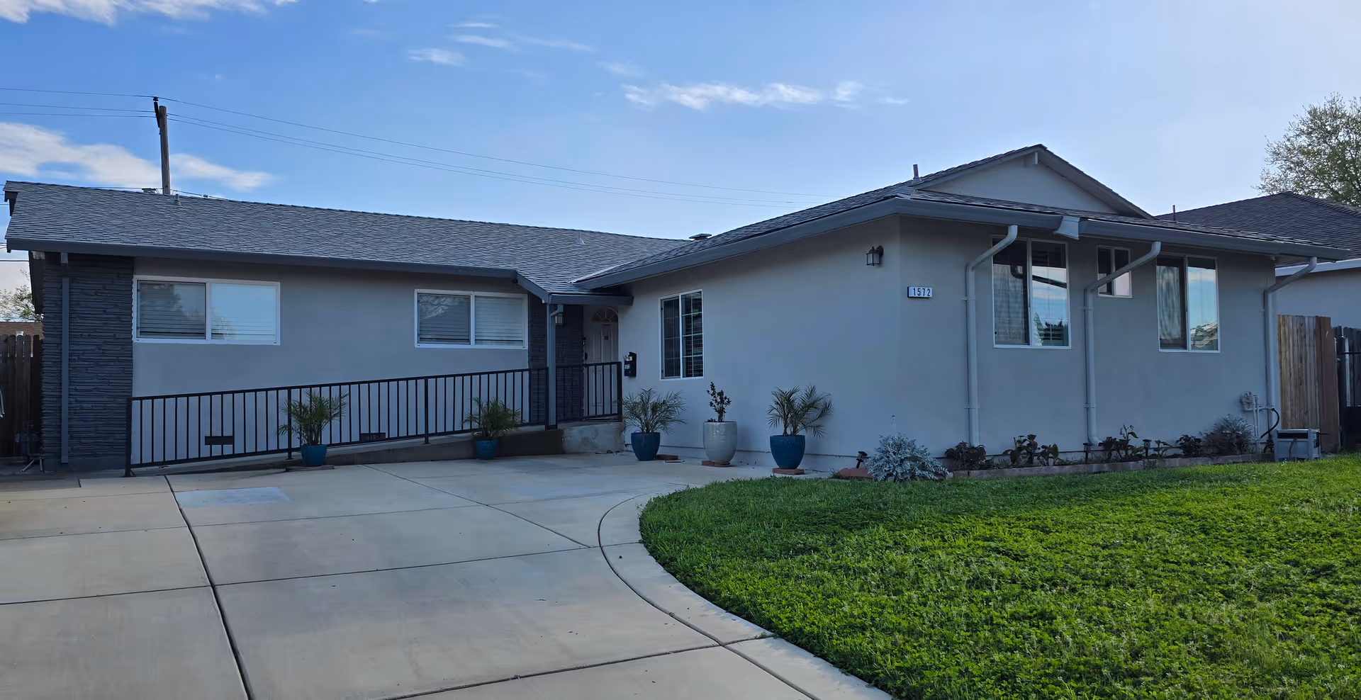 Single-story care facility front exterior with ramp and potted plants lining the entrance.