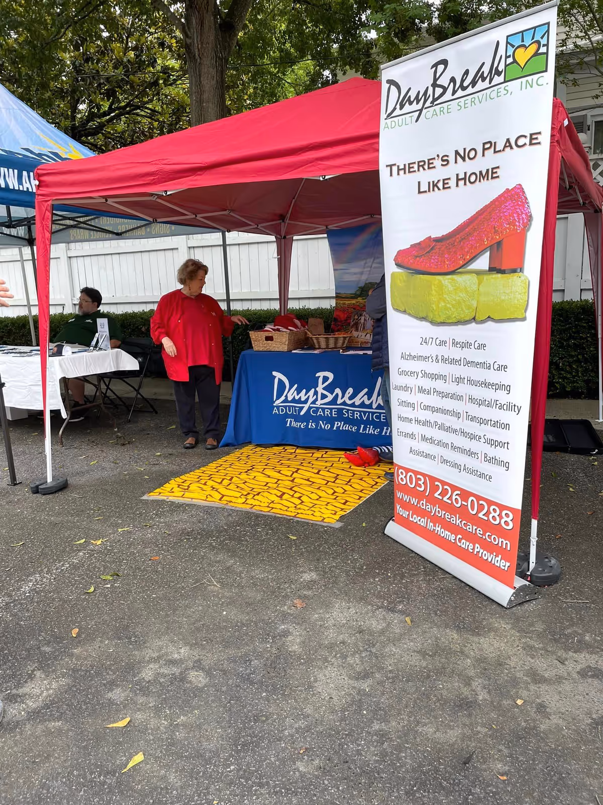 Outdoor DayBreak booth under red tent, banner and two people at a table.
