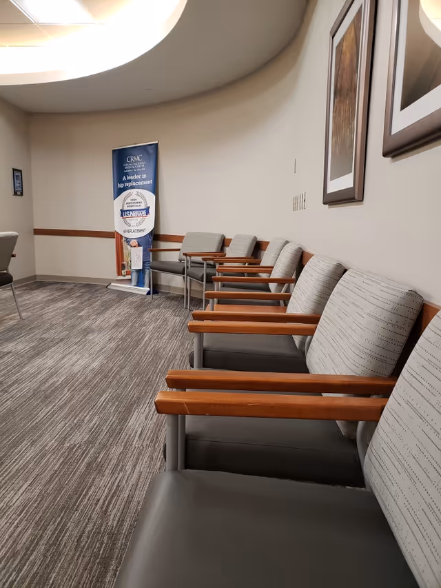 Row of gray chairs with wooden armrests in a carpeted waiting room.