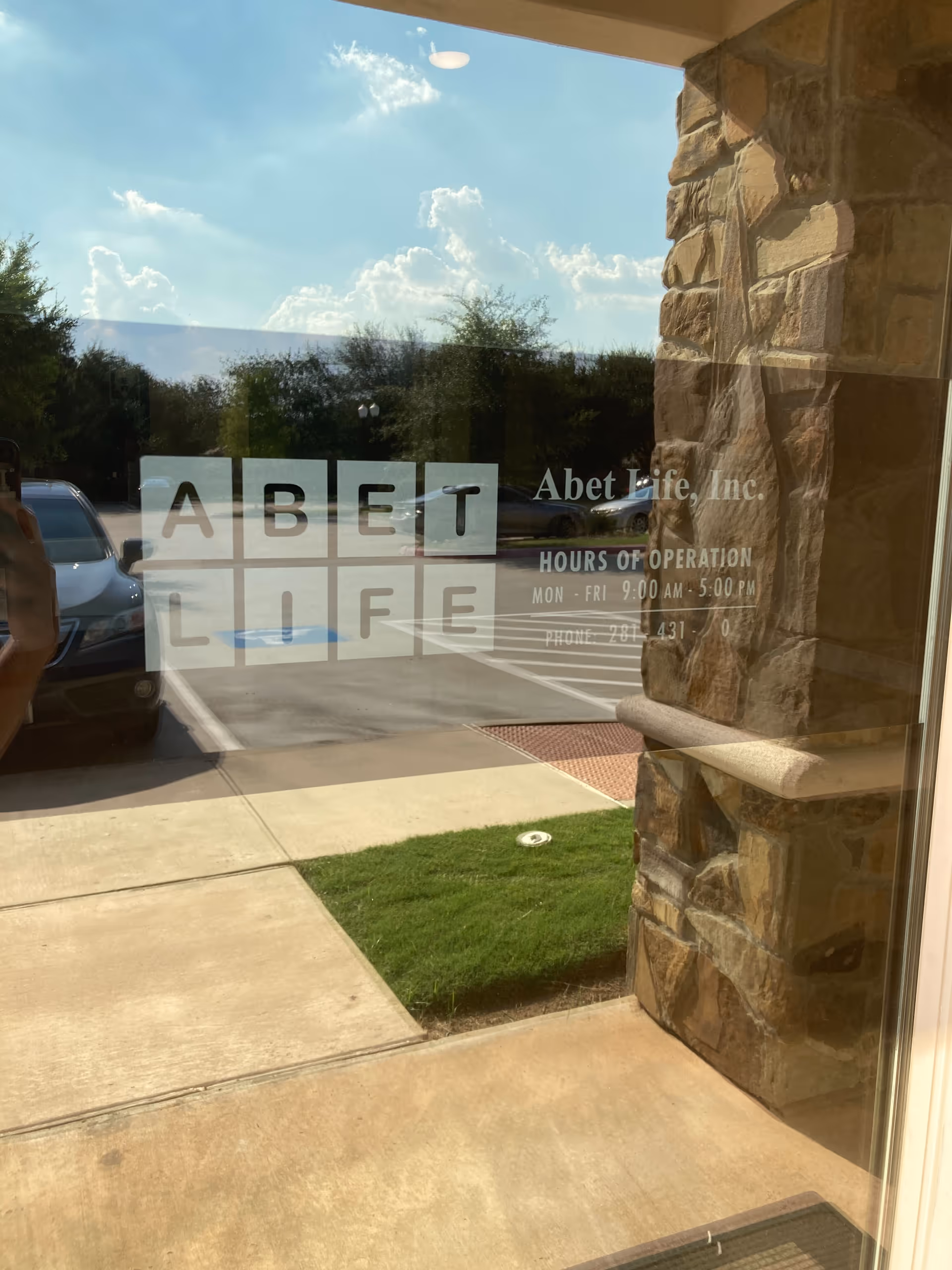 Glass storefront shows ABET Life logo with stone exterior and parked cars outside.