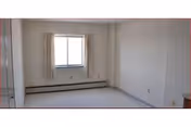Empty bedroom with a window, curtains, and a baseboard heater.