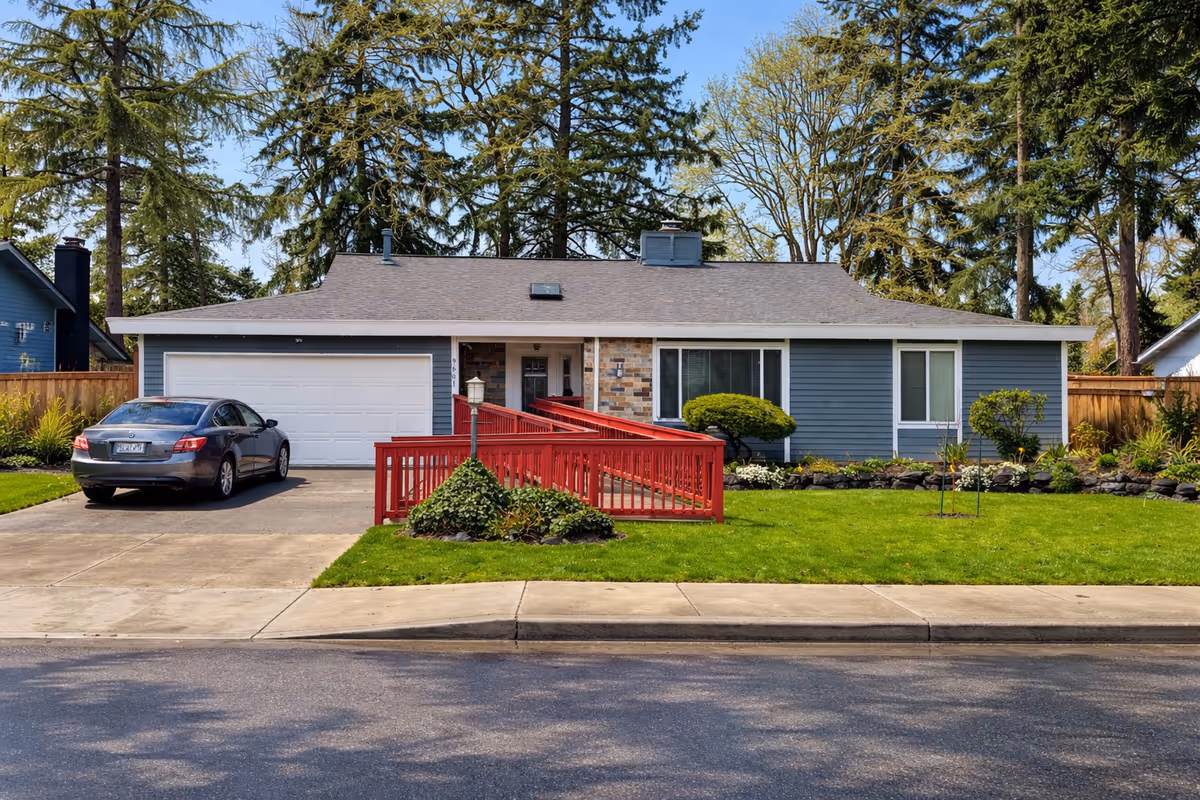 Front view of a single-story blue house with a red ramp, driveway, and lawn