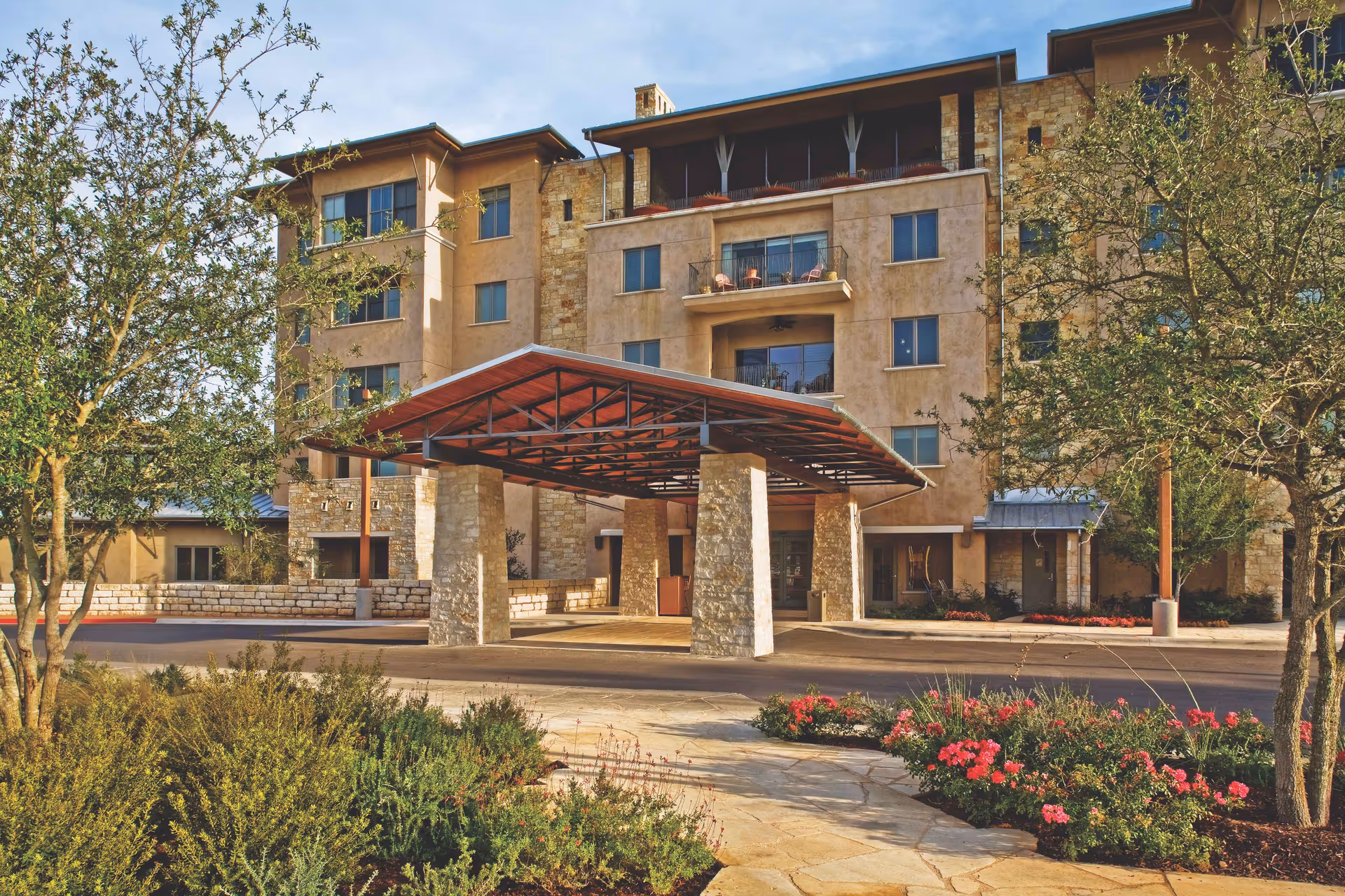 Exterior view of a multi-story senior living facility with a stone entrance and landscaped grounds.