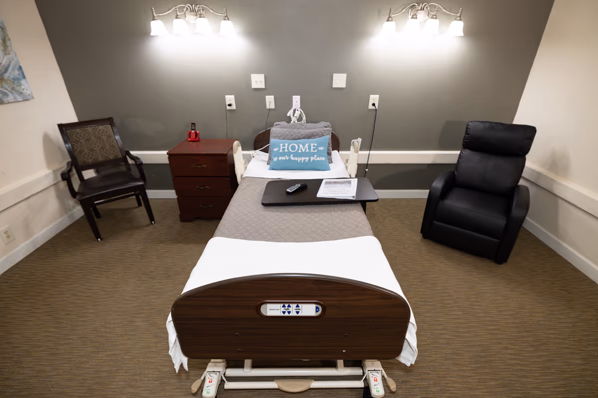A hospital-style patient bed in a small room with a recliner and chair.