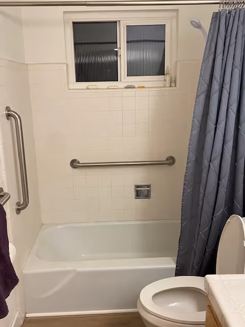 Bathroom with tub, shower curtain, grab bars, and a toilet.