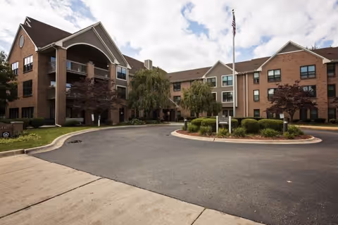 Brick senior living building with arched entrance, circular driveway, and landscaped entryway.