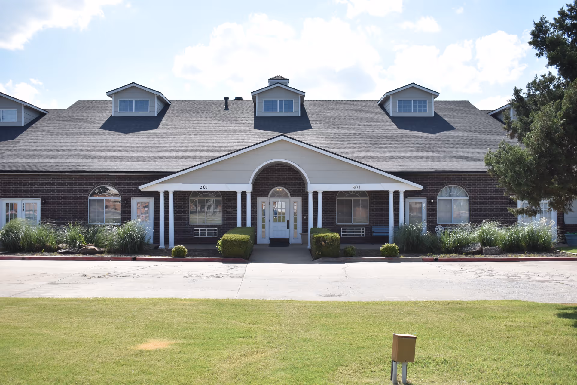 Front view of a brick assisted living facility with white columns and manicured lawn.