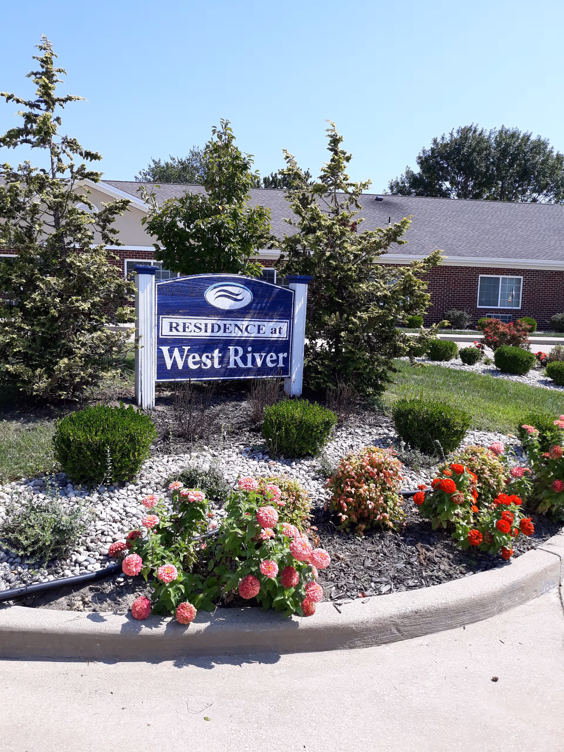 Sign reading Residence at West River sits among landscaped bushes in front of a brick building.
