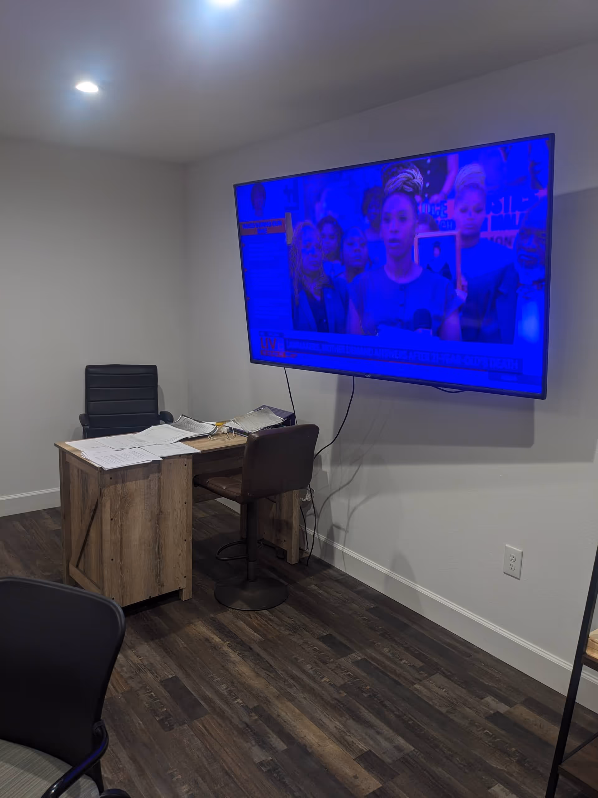Office-style room with desk, scattered papers, and a large mounted TV showing blue image.