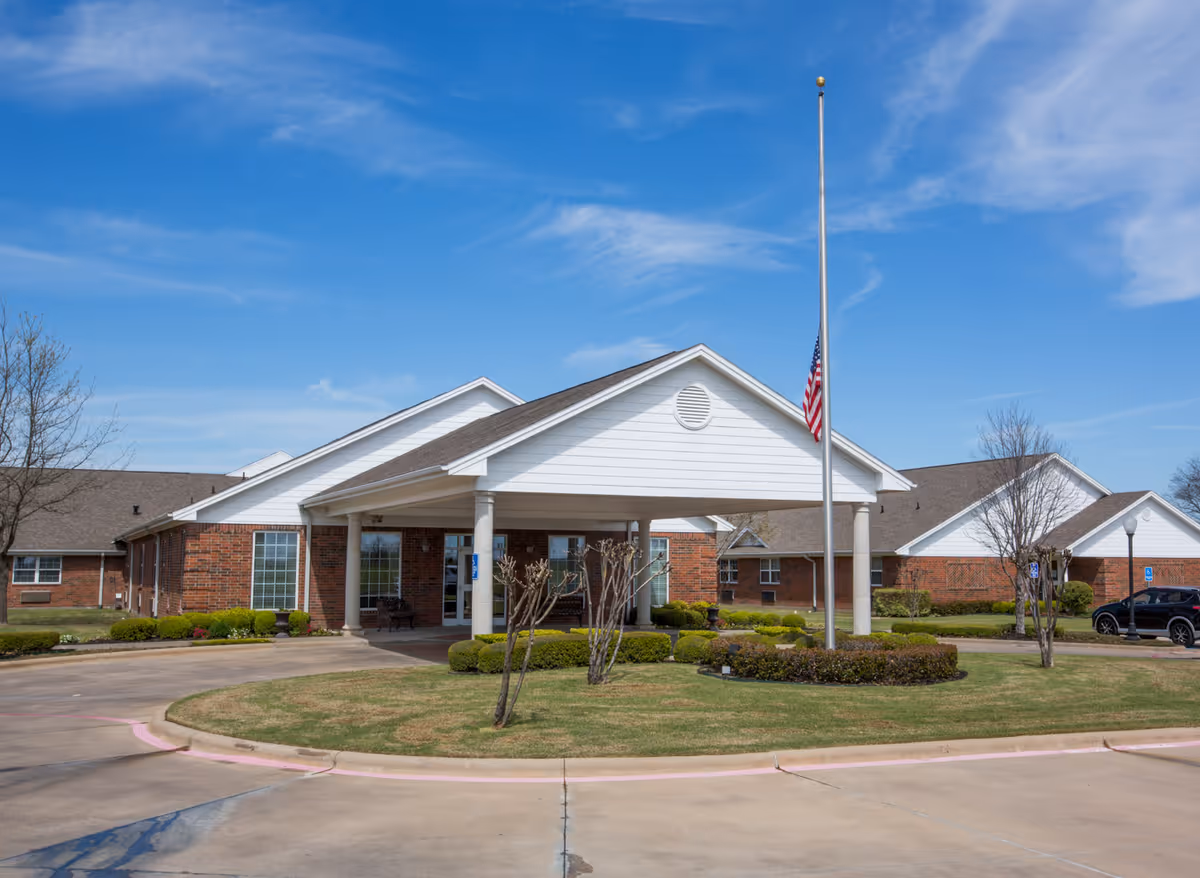 Front entrance of a single-story brick building with a covered portico and an American flag at half-staff.