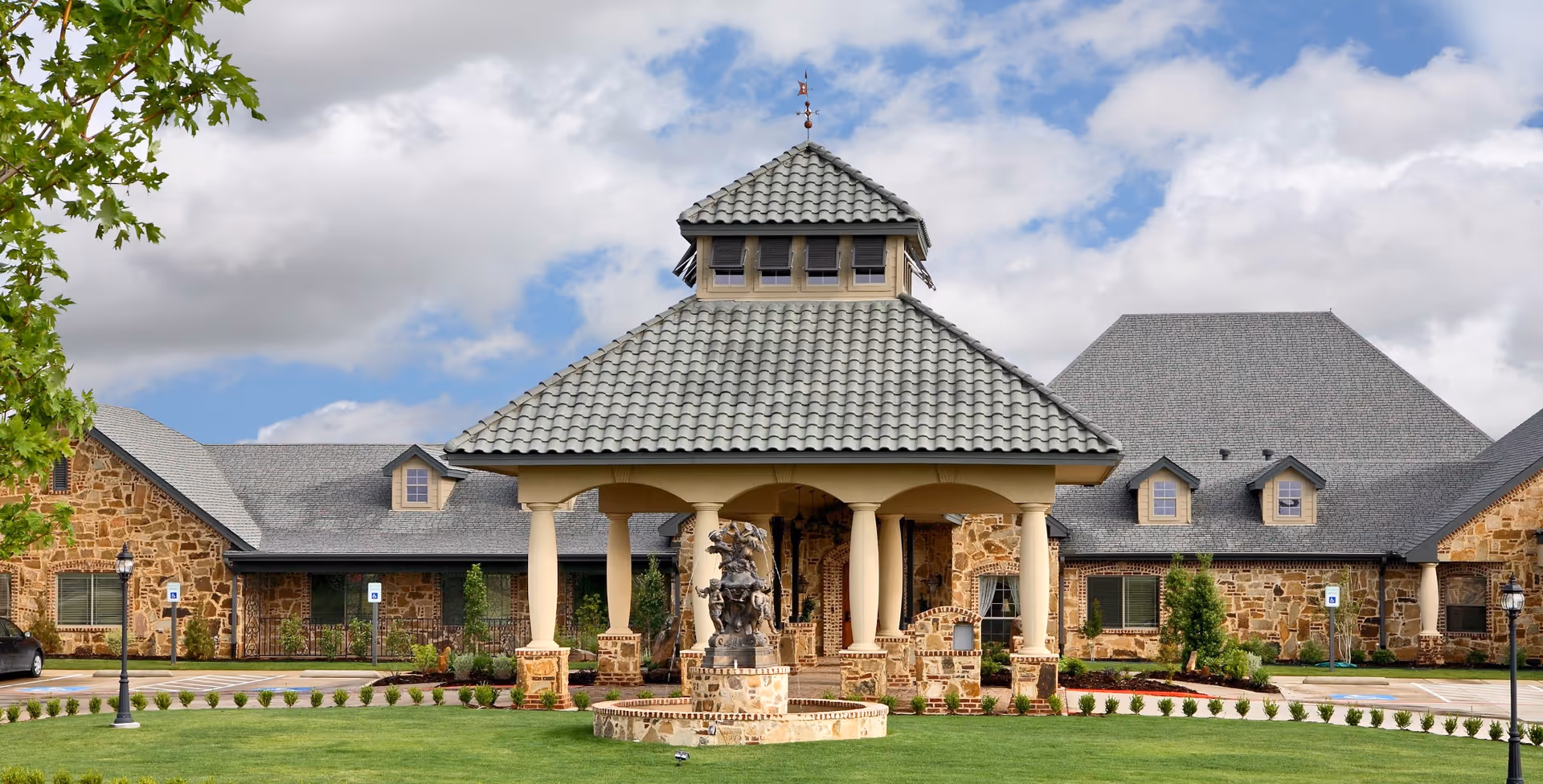 Stone-clad senior living center exterior with a central covered entrance and fountain.